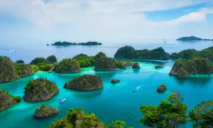Rajskie krajobrazy Raja Ampat: turkusowa woda, bujna zieleń i łodzie sunące po spokojnym morzu.