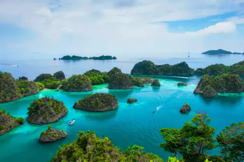 Rajskie krajobrazy Raja Ampat: turkusowa woda, bujna zieleń i łodzie sunące po spokojnym morzu.