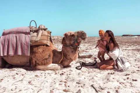 Djerba plaże: matka z dzieckiem i wielbłąd na piasku pod błękitnym niebem.