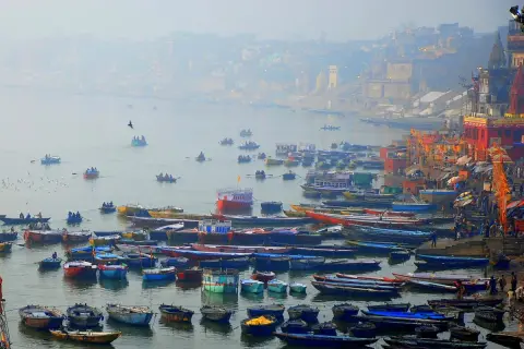 Łodzie na rzece Ganges, w tle mgliste miasto z budynkami i świątyniami.