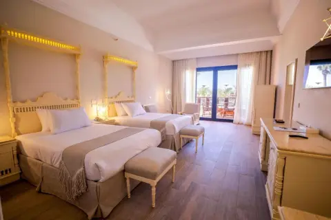 Pokój hotelowy z dwoma łóżkami, ozdobnymi zagłówkami i wyjściem na balkon. Idealne miejsce na wakacyjny calimera.
