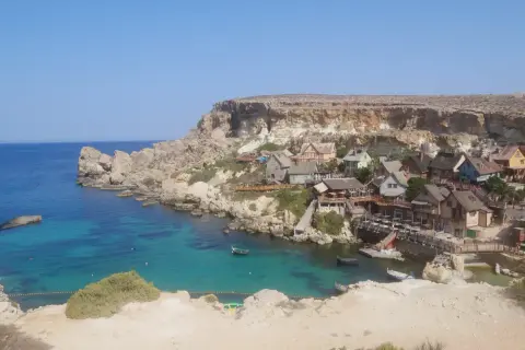 Malta zwiedzanie: kolorowa wioska rybacka w zatoce z turkusową wodą i klifami.