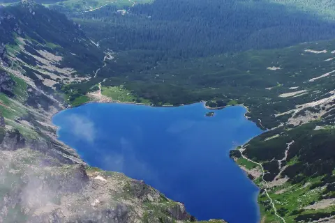 Górski staw gąsienicowy otoczony zielonymi zboczami i lasem.