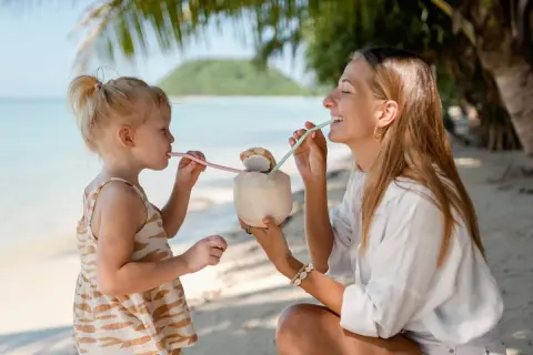 Mama i dziecko piją kokosa na plaży w Sanur. Słoneczny dzień, palmy i ocean tworzą rajską atmosferę.