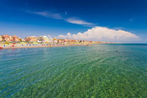 Słoneczny dzień nad morzem w Rzymie. Plaża pełna kolorowych leżaków i parasoli, ludzie kąpią się w krystalicznie czystej wodzie.