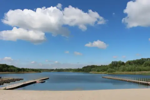 Piękny dzień nad Jeziorem Wilcze Wielkopolskie. Piaszczysta plaża, drewniane pomosty i błękitne niebo z białymi chmurami zapraszają do wypoczynku.