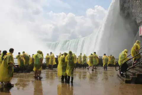 Tłum turystów w żółtych płaszczach przeciwdeszczowych podziwia potęgę wodospadu Niagara. Ciekawe informacje o tym miejscu czekają na odkrycie.