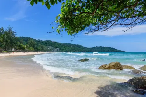 Piękna plaża Kata Beach z turkusową wodą, falami i zielonymi wzgórzami w tle. Idealne miejsce na relaks.