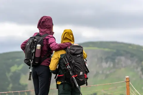 Dwie osoby w kurtkach z kapturem i plecakami patrzą na krajobraz.