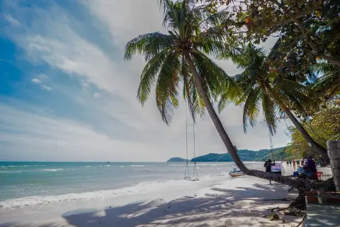 Huśtawka pod palmą na rajskiej sao beach. W tle turkusowe morze i zielone wzgórza.