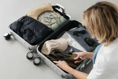 Pakowanie walizki na podróż samolotem: kurtka, torebka, bielizna, czapka, buty, okulary i perfumy.