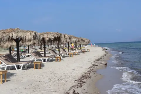 Piękna plaża Tigaki z rzędami leżaków pod słomianymi parasolami, spokojne morze i błękitne niebo.