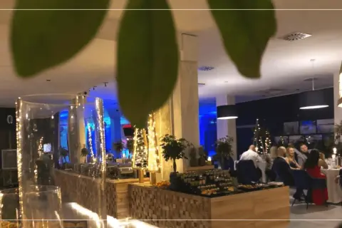 Elegancki sylwester w hotelu. Goście siedzą przy stołach, w tle bufet z przekąskami i świąteczne dekoracje.