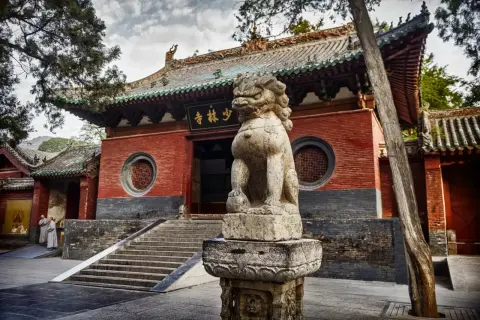 Kamienny lew strzeże wejścia do klasztoru Shaolin. Dwie postacie w szatach mnichów zbliżają się do schodów.