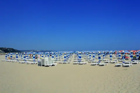 Plaża w Albena Bułgaria, rzędy leżaków i parasoli w niebiesko-białe pasy pod błękitnym niebem.