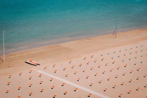 Pusta plaża w Rimini z rzędem pomarańczowych parasoli i małą łodzią motorową.