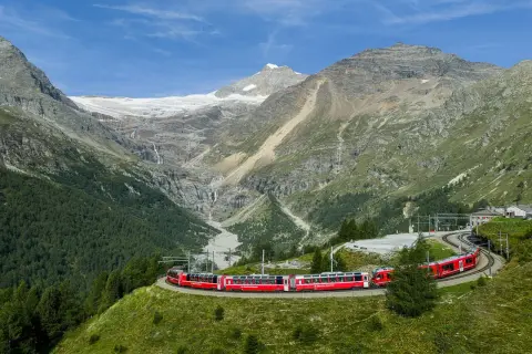 Czerwony pociąg Bernina Express w Szwajcarii pokonuje malowniczą trasę wśród górskich krajobrazów z lodowcem i wodospadami.