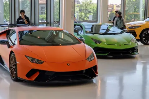 Pomarańczowy i zielony Lamborghini w muzeum Lamborghini. Obok żółty SUV.