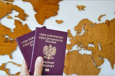 Dwa polskie paszporty na tle drewnianej mapy świata. Zastanawiasz się, ile kosztuje paszport tymczasowy?