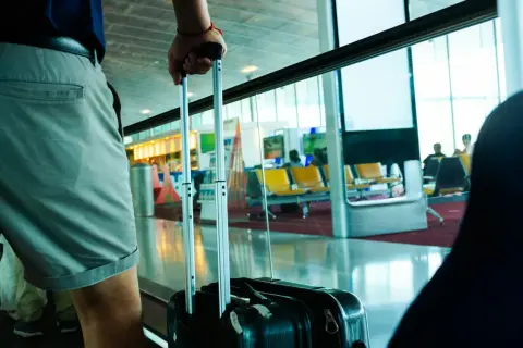 Osoba z walizką czeka na loty do Chin na lotnisku. W tle widać poczekalnię z żółtymi siedzeniami.