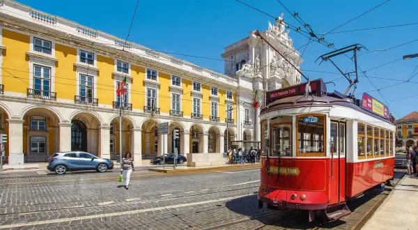 Czerwony tramwaj w Lizbonie, obok żółtego budynku z arkadami. Czy do Portugalii potrzebny jest paszport? Tak, jeśli nie jesteś obywatelem UE.