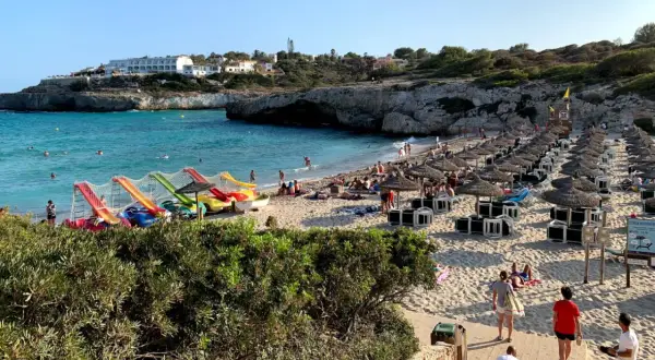 Słoneczna plaża Cala Domingos z kolorowymi zjeżdżalniami wodnymi, rzędami parasoli i turystami cieszącymi się słońcem i morzem.