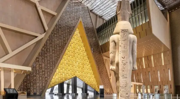 Wielki posąg faraona w nowoczesnym muzeum egipskim. Ściany zdobią hieroglify i złote panele.