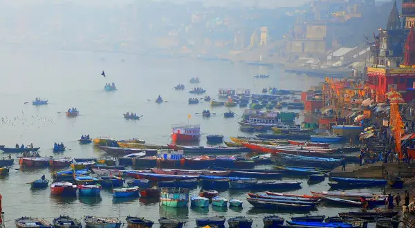 Łodzie na rzece Ganges, w tle mgliste miasto z budynkami i świątyniami.