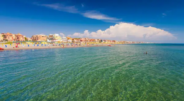 Słoneczny dzień nad morzem w Rzymie. Plaża pełna kolorowych leżaków i parasoli, ludzie kąpią się w krystalicznie czystej wodzie.