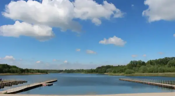 Piękny dzień nad Jeziorem Wilcze Wielkopolskie. Piaszczysta plaża, drewniane pomosty i błękitne niebo z białymi chmurami zapraszają do wypoczynku.