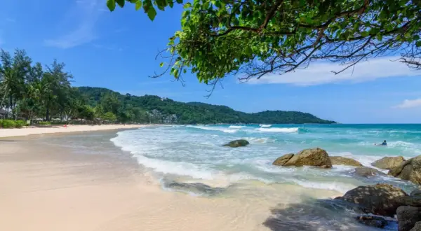 Piękna plaża Kata Beach z turkusową wodą, falami i zielonymi wzgórzami w tle. Idealne miejsce na relaks.