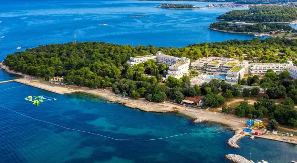 Hotel Delfin Plava Laguna, otoczony zielenią, z basenami i plażą nad turkusowym morzem.