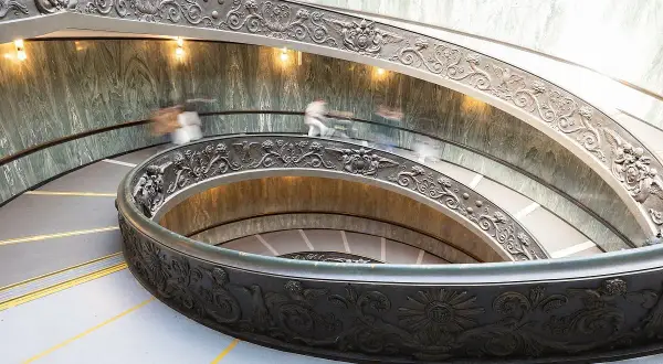 Watykańska, spiralna klatka schodowa z bogatymi zdobieniami, gdzie ludzie spieszą na audiencję u papieża.