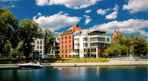 Nowoczesne budynki nad wodą, przypominające hotel Almond, z łodzią przy nabrzeżu i błękitnym niebem.
