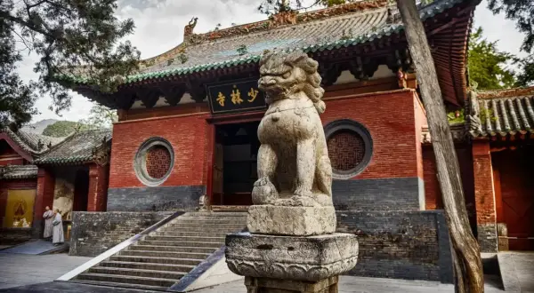 Kamienny lew strzeże wejścia do klasztoru Shaolin. Dwie postacie w szatach mnichów zbliżają się do schodów.