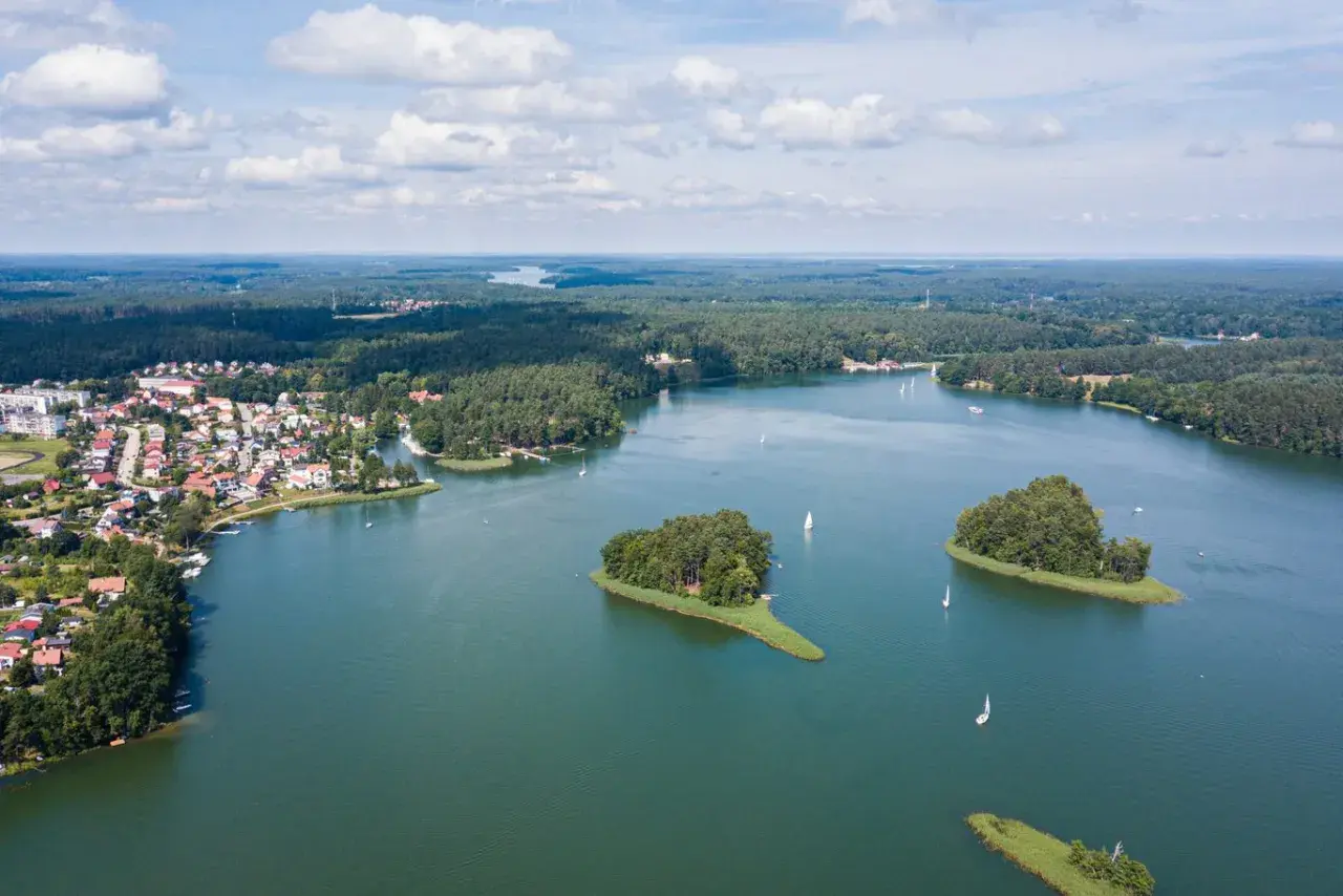 Malownicze jeziora w Polsce na wakacje. Widok z lotu ptaka na miasteczko nad wodą, wyspy porośnięte drzewami i żaglówki.