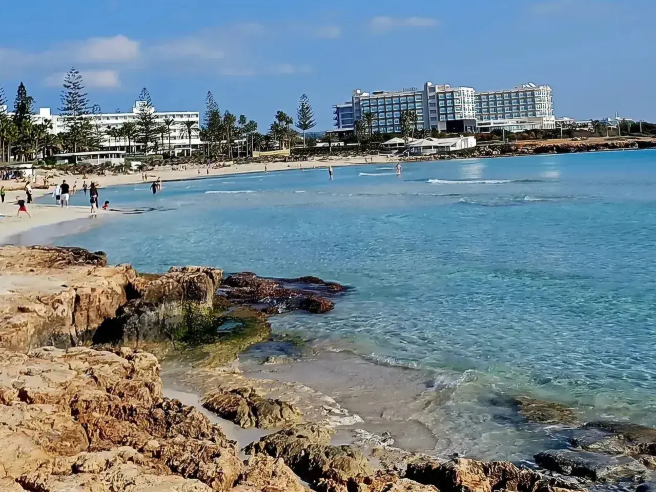 Słoneczny dzień na plaży Ayia Napa. Turkusowa woda, piaszczysty brzeg i hotele w tle.