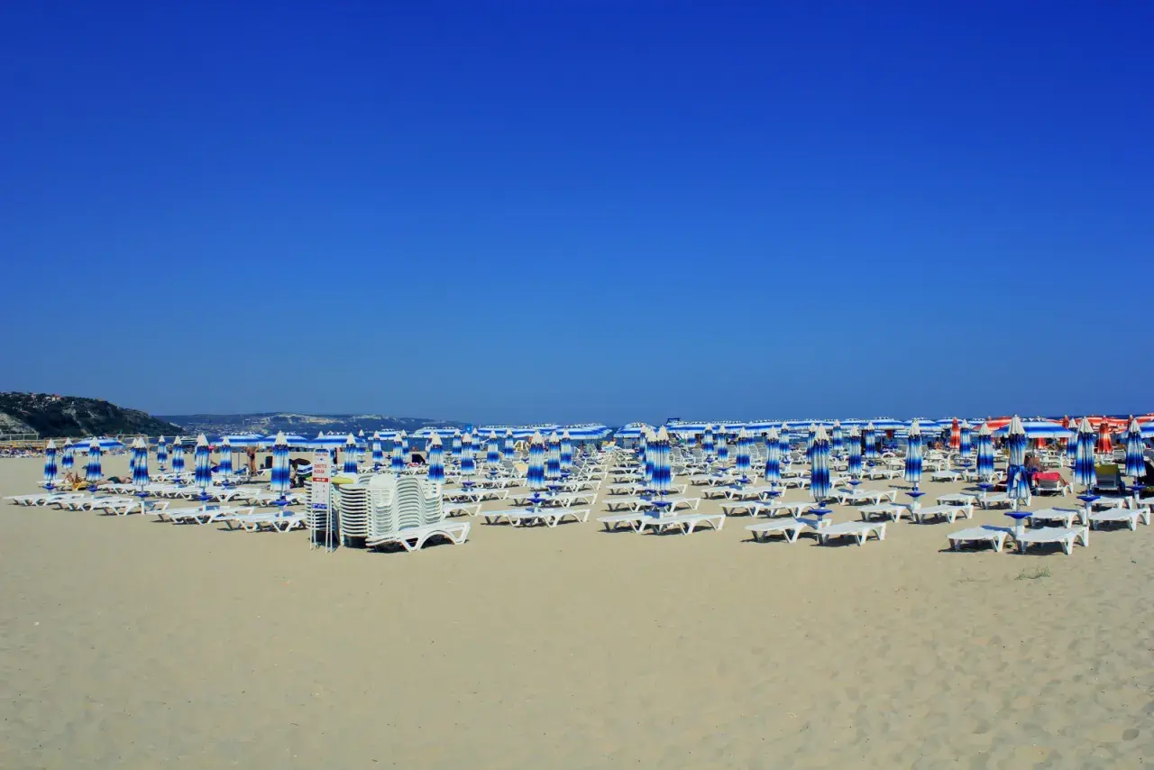 Plaża w Albena Bułgaria, rzędy leżaków i parasoli w niebiesko-białe pasy pod błękitnym niebem.