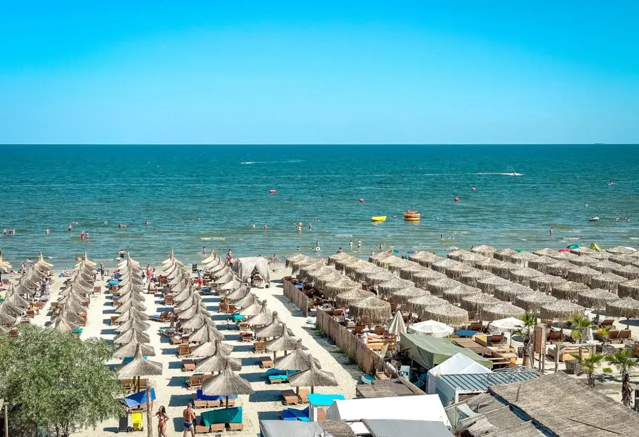 Słoneczny kurort nad Morzem Czarnym tętni życiem. Plaża pełna leżaków i parasoli, a w wodzie kąpią się ludzie.
