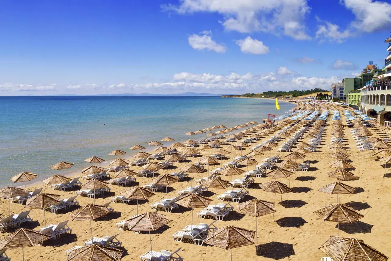 Słoneczna plaża w Bułgarii, idealna na 10 dni samolotem. Rzędy leżaków i parasoli czekają na turystów.