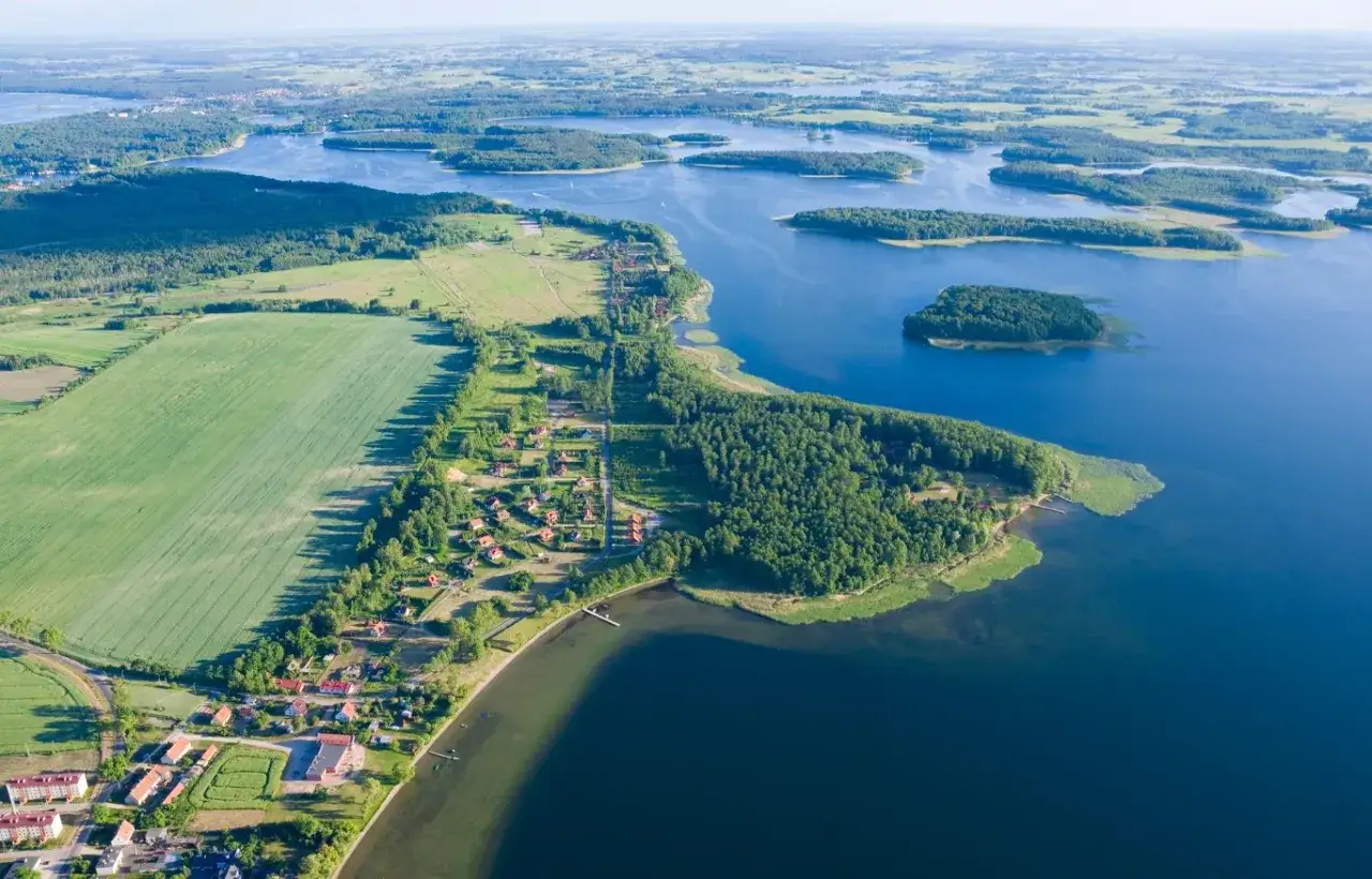Malownicze jezioro Jegocin z licznymi wyspami, otoczone lasami i polami. Widoczne domy letniskowe i zabudowania.