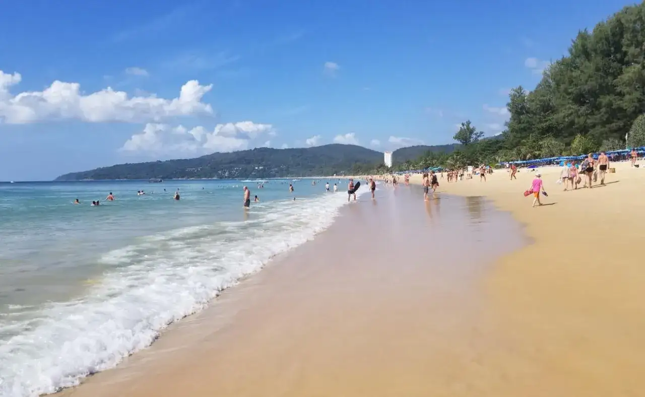 Słoneczny dzień na plaży Karon. Ludzie kąpią się w turkusowej wodzie i spacerują po złotym piasku.