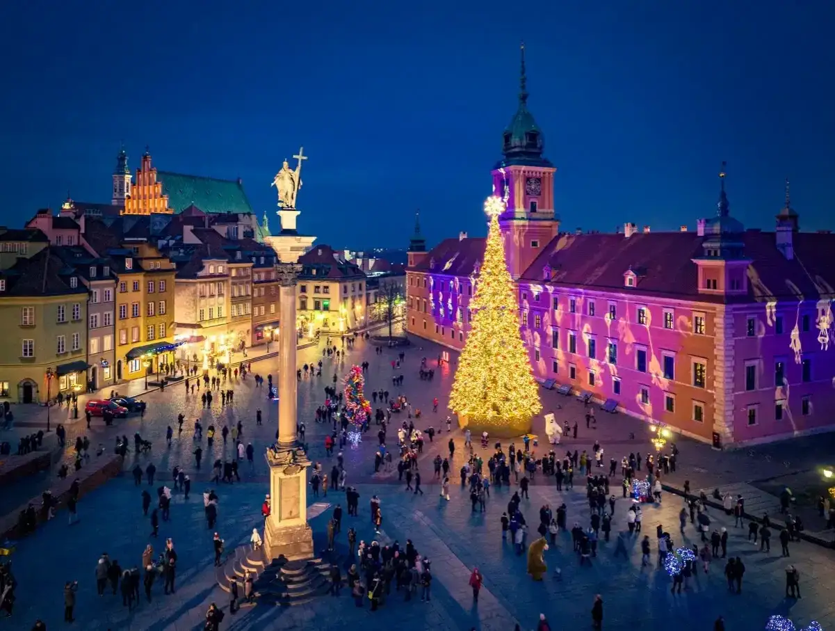 Świąteczne atrakcje Warszawy dzisiaj: Plac Zamkowy rozświetlony choinką i iluminacjami, tłumy spacerują wśród zabytkowych kamienic.
