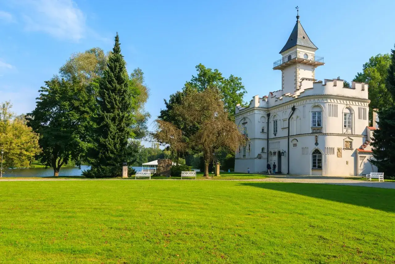Biały pałac z wieżą, otoczony zielenią i jeziorem, to jeden z urokliwych zamków na Mazowszu.