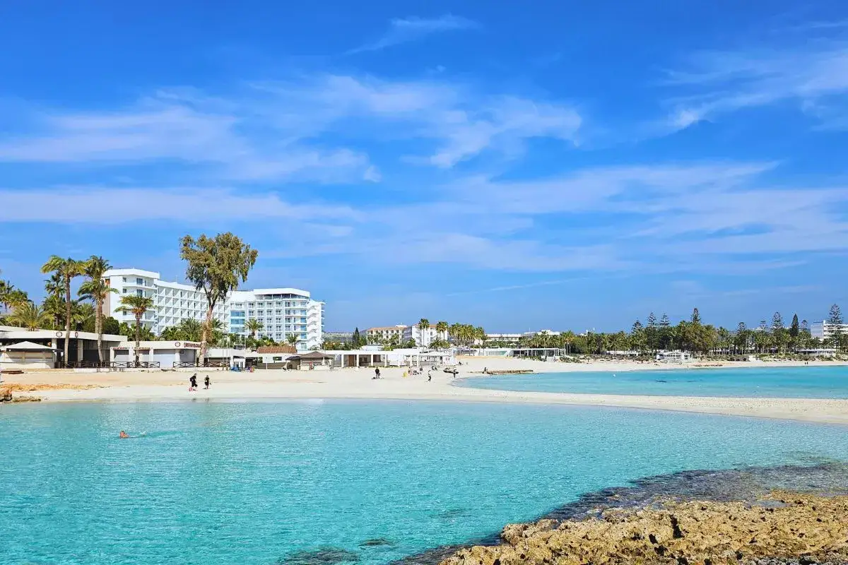 Piękny, turkusowy ocean na plaży Ayia Napa, z białymi hotelami i palmami w tle.