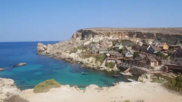 Malta zwiedzanie: kolorowa wioska rybacka w zatoce z turkusową wodą i klifami.