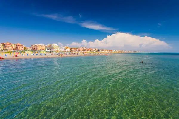 Słoneczny dzień nad morzem w Rzymie. Plaża pełna kolorowych leżaków i parasoli, ludzie kąpią się w krystalicznie czystej wodzie.