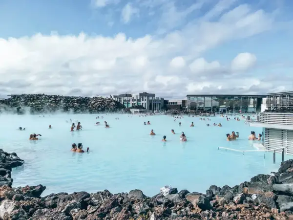 Relaks w Blue Lagoon, geotermalnym spa na Islandii. Ludzie kąpią się w mlecznoniebieskiej wodzie, otoczeni wulkanicznymi skałami i nowoczesną architekturą.