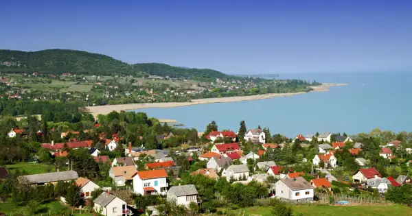 Widok na malowniczą wieś nad jeziorem Balaton. Domy z czerwonymi dachami, zielone wzgórza i błękitna woda tworzą idylliczny krajobraz. Idealne miejsce na wakacje nad Balatonem.