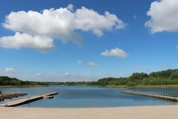 Piękny dzień nad Jeziorem Wilcze Wielkopolskie. Piaszczysta plaża, drewniane pomosty i błękitne niebo z białymi chmurami zapraszają do wypoczynku.